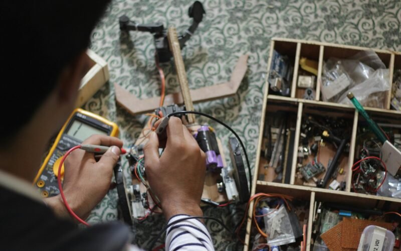 Man soldering electronic parts at a table filled with tools and equipment.