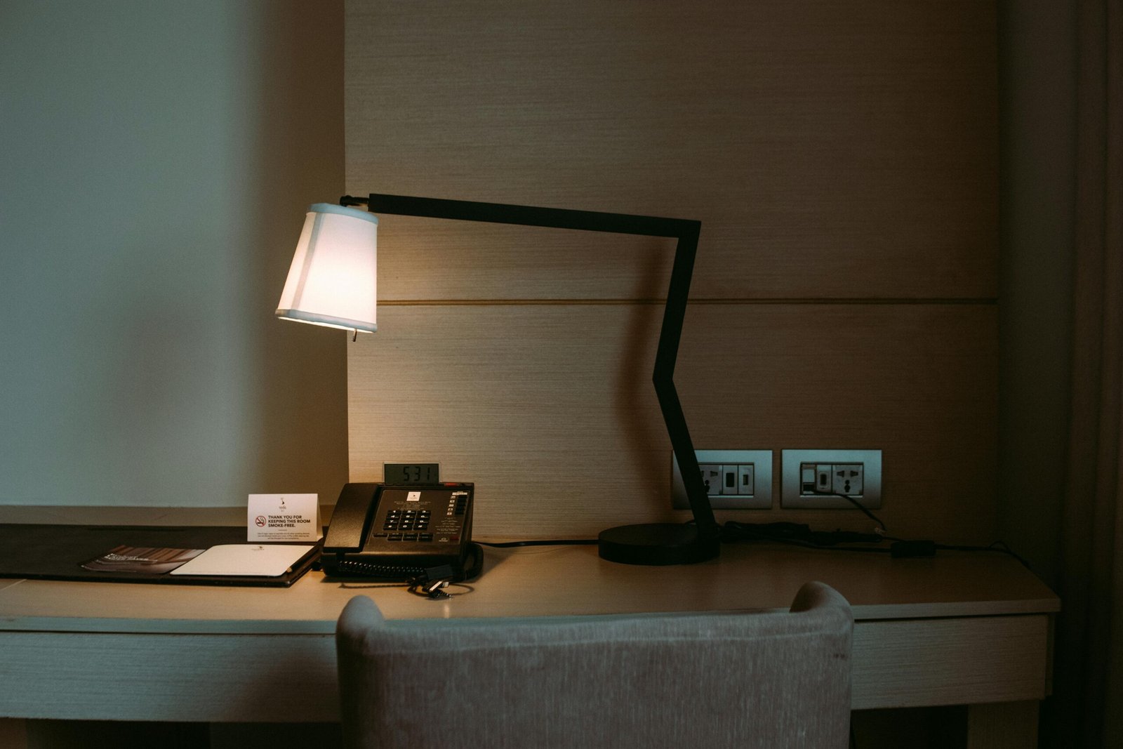 A modern hotel room desk featuring a stylish lamp, telephone, and stationery set.
