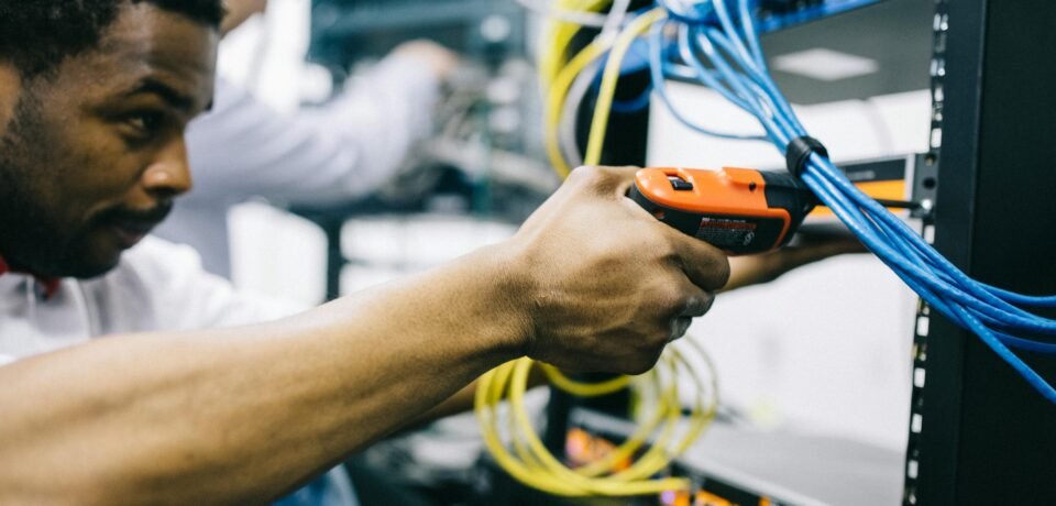 Side view crop concentrated African American engineer repairing equipment by using electric screwdriver