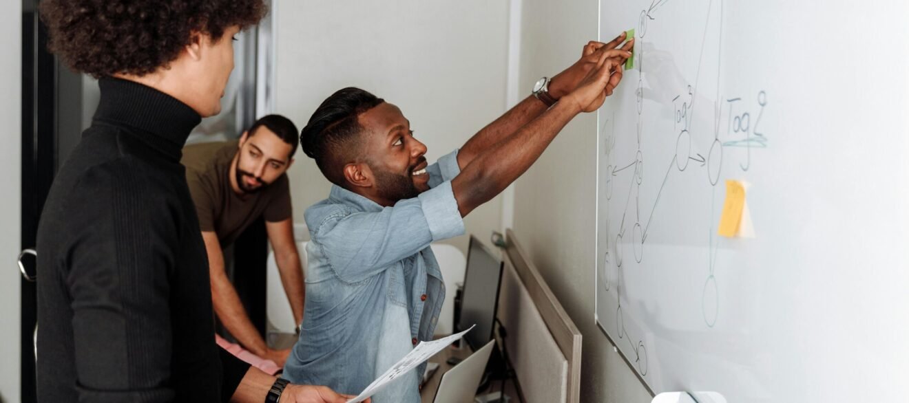 A diverse team of professionals brainstorming solutions at a whiteboard in an office setting.