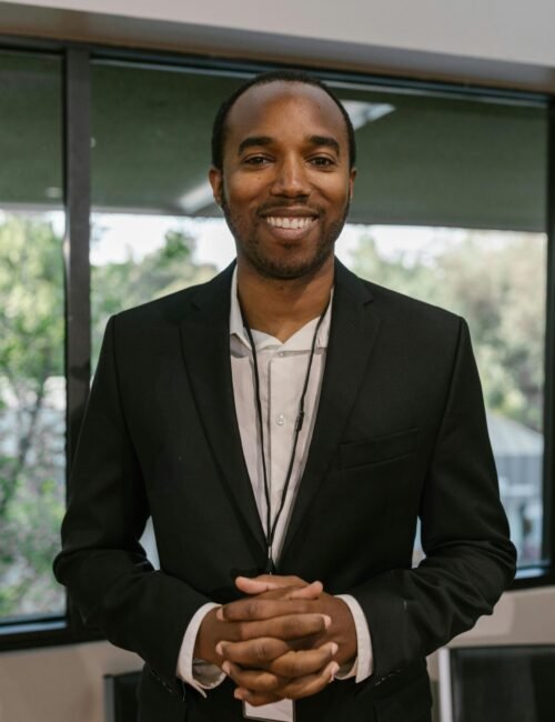 Smiling businessman in black blazer standing confidently indoors.
