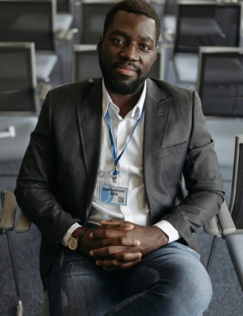 African American man in a gray suit sitting confidently in a conference setting.